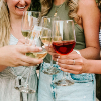 A group of women clinking glasses filled with white and red wine, smiling and enjoying a celebratory moment.